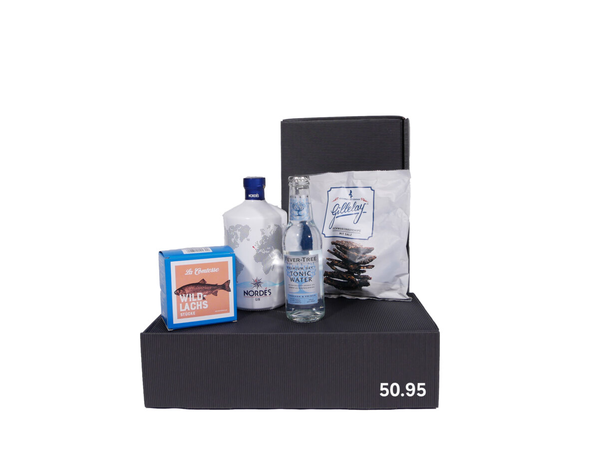 Geschenkbox mit einer Flasche Gin, einer kleinen Flasche Tonic Water, einer Packung Wildlachs und einer Tüte Kartoffelchips auf gestreiftem Hintergrund.
