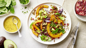 Ein Teller mit einem Linsensalat, der Kürbisscheiben, Granatapfelkerne, rote Zwiebeln und frischen Spinat enthält.